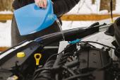 Car maintenance. Man pouring car winter windshield washer fluid outdoor. Closeup image taken outdoors. Man pouring car winter windshield washer fluid