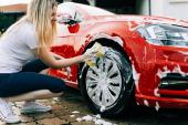 Young woman washing her car with sponge.